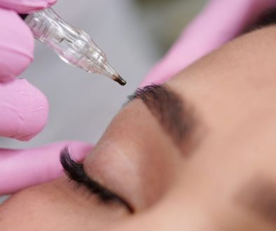 Close-up of a permanent makeup machine applying pigment to an eyebrow during a cosmetic brow tattooing treatment.