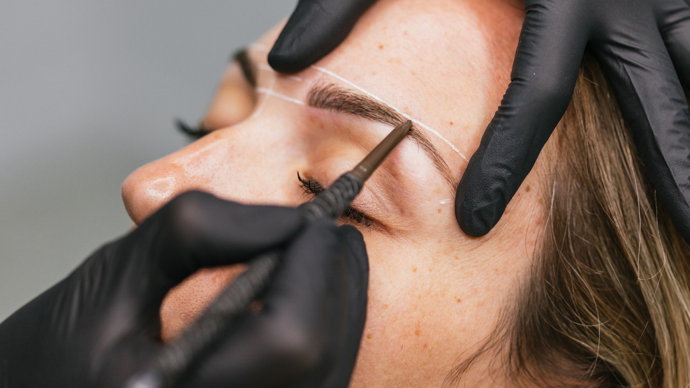 Close-up of eyebrow mapping and shaping with a cosmetic pencil before a microblading/ permanent makeup brow treatment.