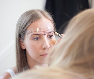 Blink Beauty Bar founder Ashley Schuh measuring and mapping a client's eyebrows with a brow ruler and pencil before a permanent makeup treatment.