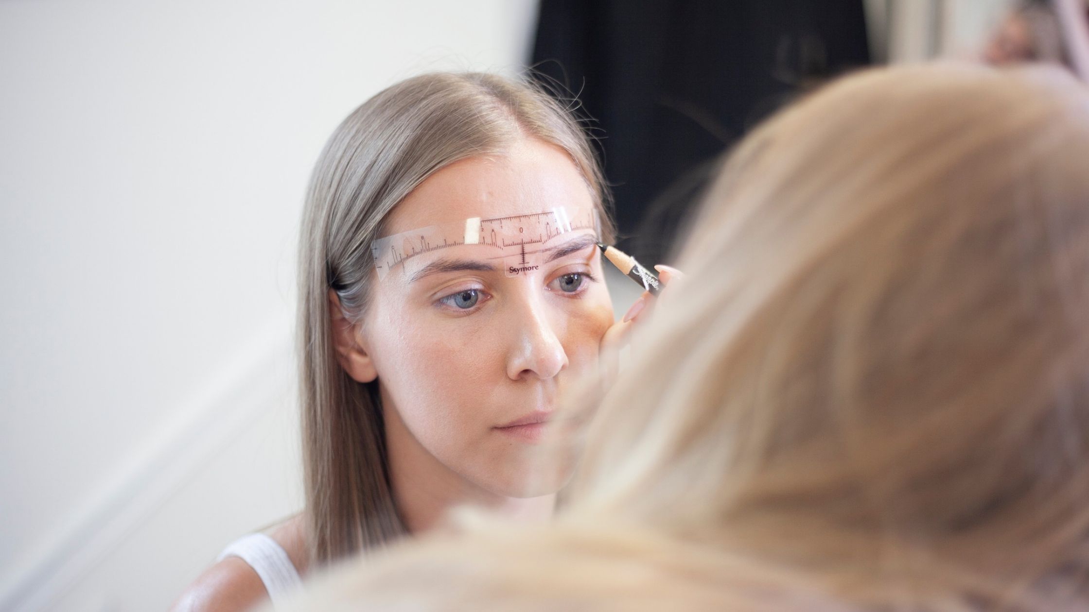Blink Beauty Bar founder Ashley Schuh measuring and mapping a client's eyebrows with a brow ruler and pencil before a permanent makeup treatment.